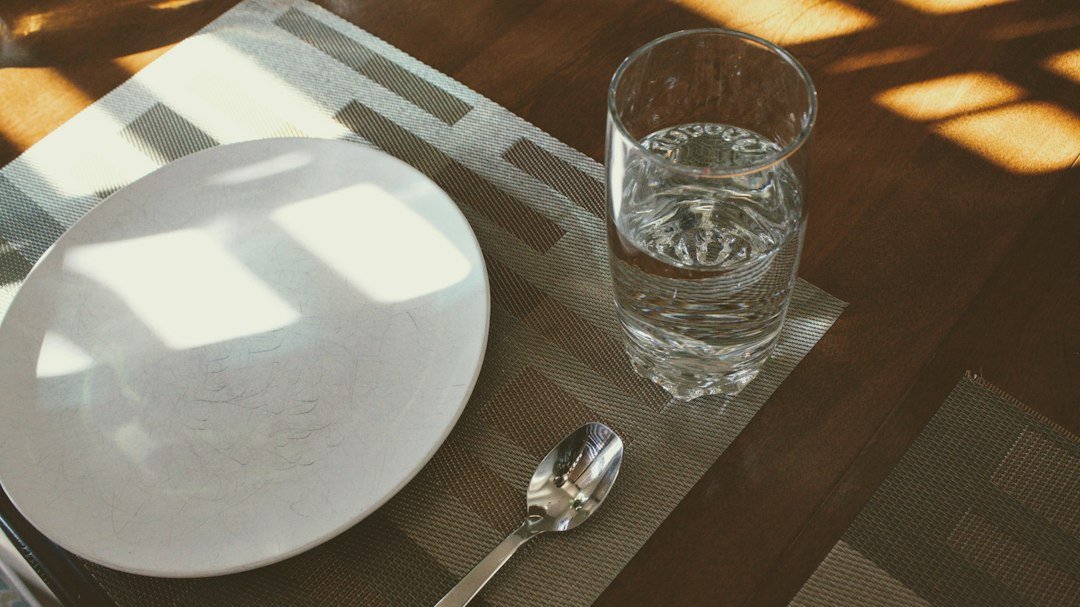 A clear glass of water beside a spoon for preparing psyllium husk